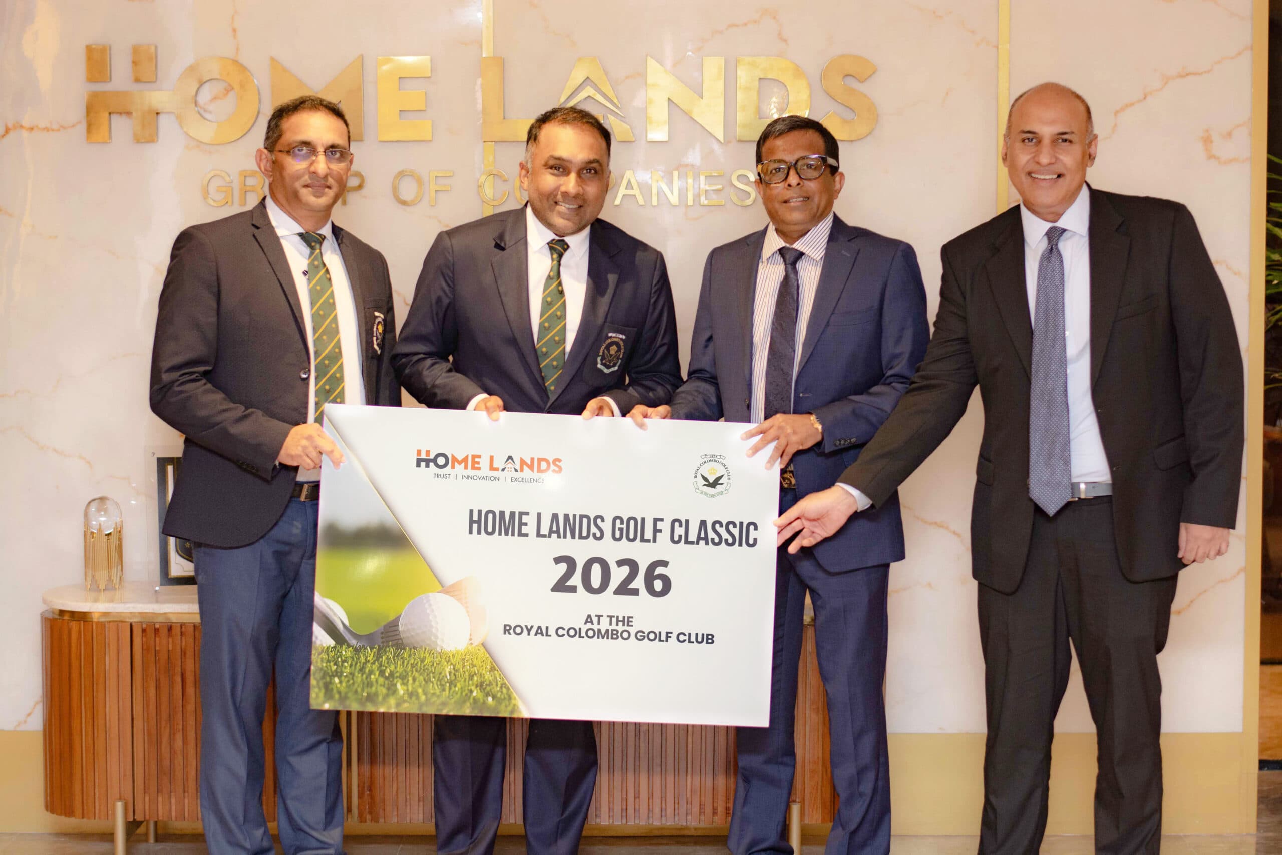 Four men in suits holding a large event banner at a golf club, posing for a photo during a formal ceremony.