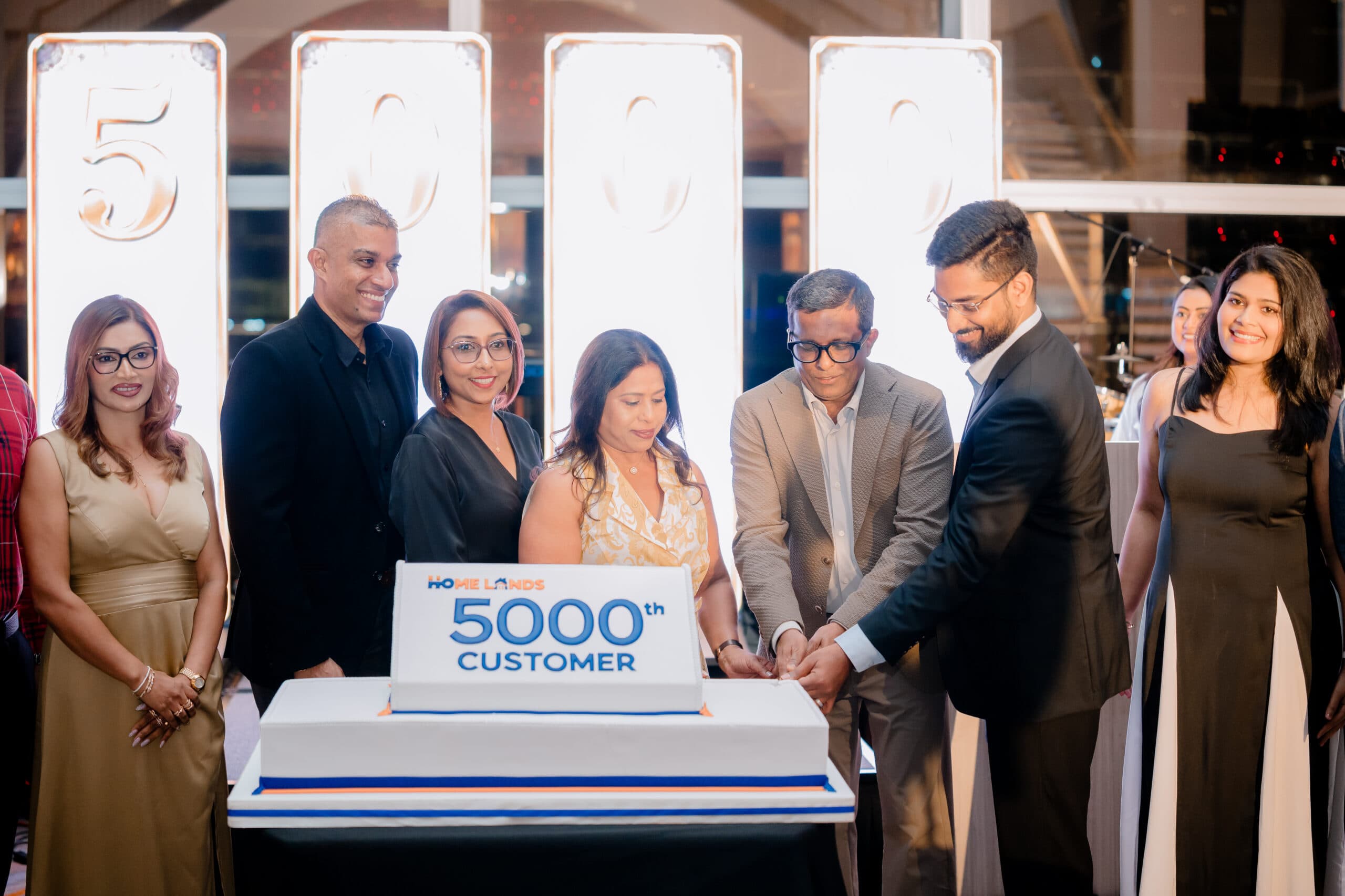 Group of professionals at a milestone celebration, cutting a cake that reads '5000th Customer'.